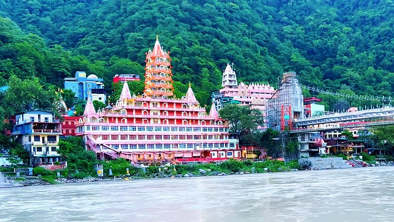 Multi‑storied Trayambakeshwar Temple with its orange towers beside Lakshman Jhula