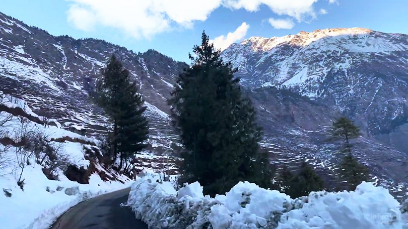 Harsil and Dharali villages in winter with snow-covered houses, trees, and riverside valley.