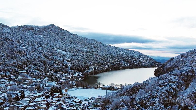 Nainital winter view with snowy hills, pine trees, and Naini Lake surroundings.