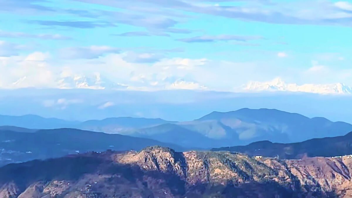 Snow-covered Himalayan mountains with clouds and a wide green valley in Mukteshwar, Uttarakhand.